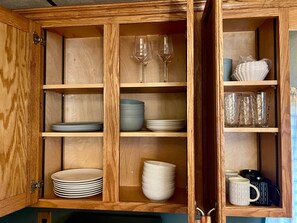 A wooden cabinet with shelves containing plates, bowls, and glasses. - Hidden Cabin Vibes | Cozy Fireplace Retreat (McMechen)