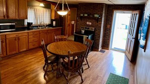 Une cuisine avec des meubles en bois, une table à manger avec des chaises, un luminaire suspendu et un mur en briques.