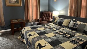 A bedroom with a large bed, a leather armchair, a small table, and a wall-mounted deer head decoration. - The Buck Lodge | Arcade • Firepit (Wheeling)