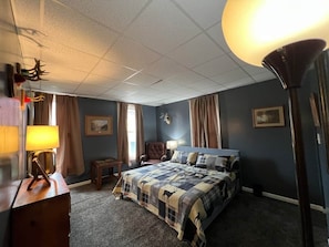 Un dormitorio con una cama, una silla, una lámpara y una decoración de cabeza de ciervo en la pared.