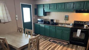 A kitchen with teal cabinets, a wooden dining table, and a black stove. - The Buck Lodge | Arcade • Firepit (Wheeling)