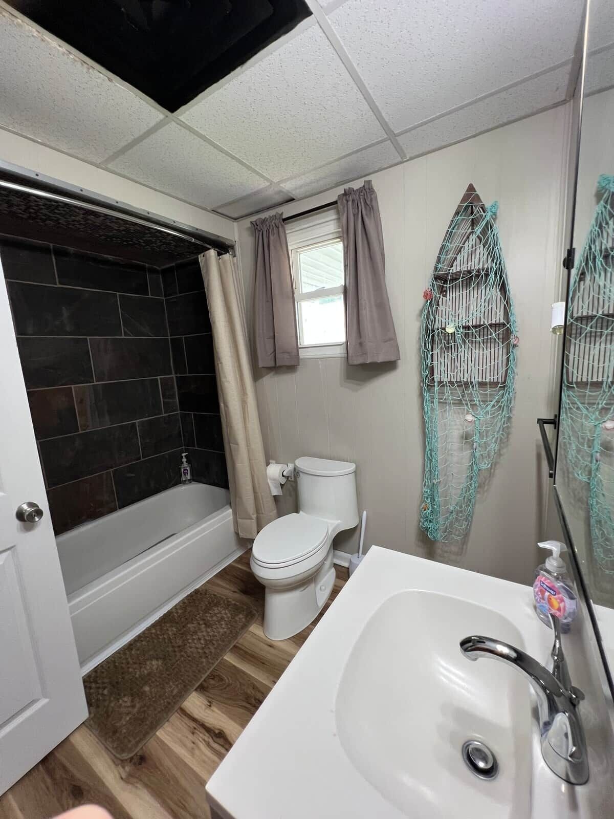 A bathroom with a bathtub, toilet, sink, and a window with curtains.