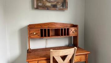 A wooden desk with a cross-back chair, a shelf above, and a wall-mounted display case.
