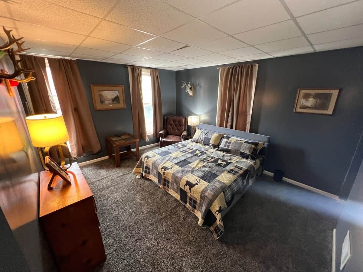 Een slaapkamer met een bed, een stoel, een lamp en een aan de muur bevestigd decoratie van een hertenhoofd.