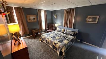 Een slaapkamer met een bed, een stoel, een lamp en een aan de muur bevestigd decoratie van een hertenhoofd.
