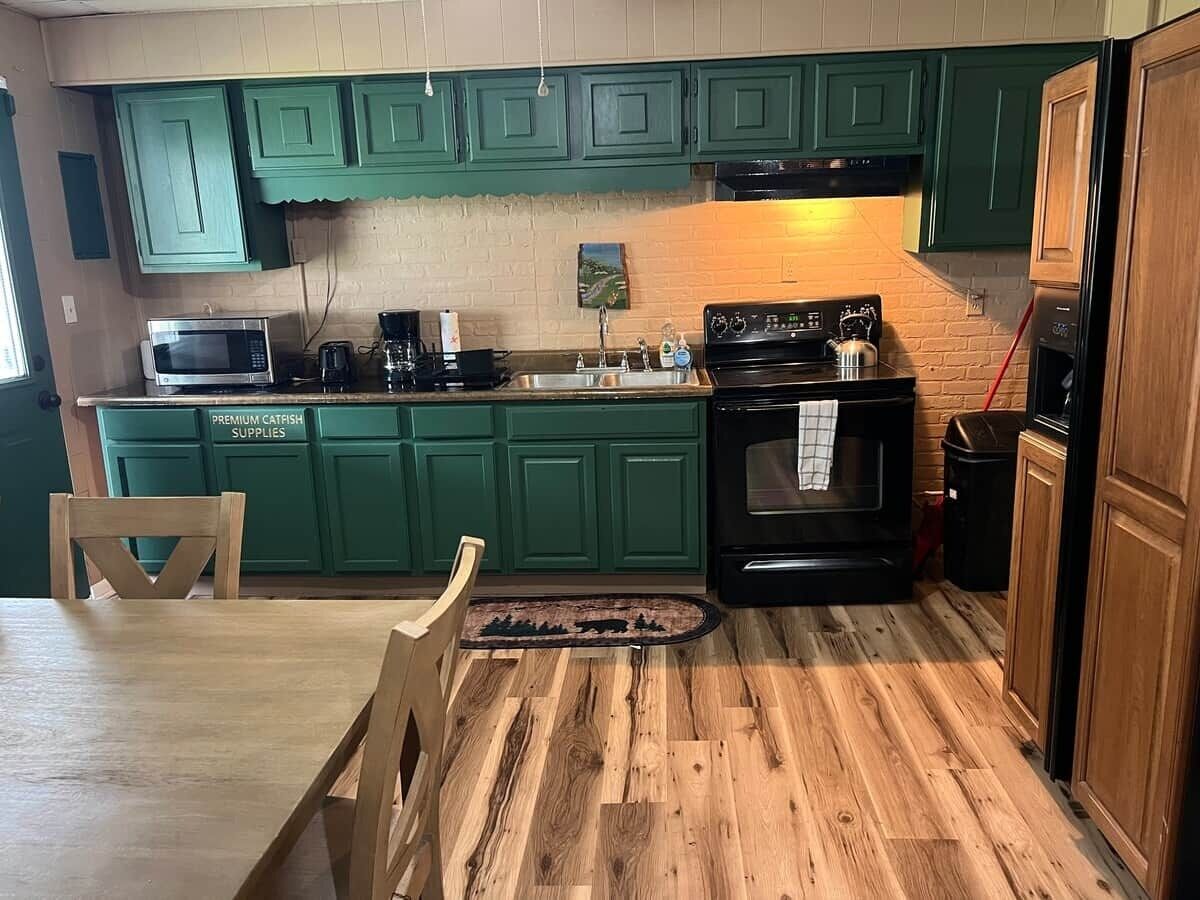 A kitchen with green cabinets, a microwave, a stove, and a dining table with chairs.