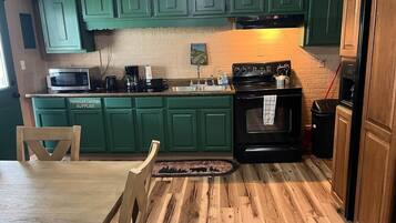 A kitchen with green cabinets, a microwave, a stove, and a dining table with chairs.