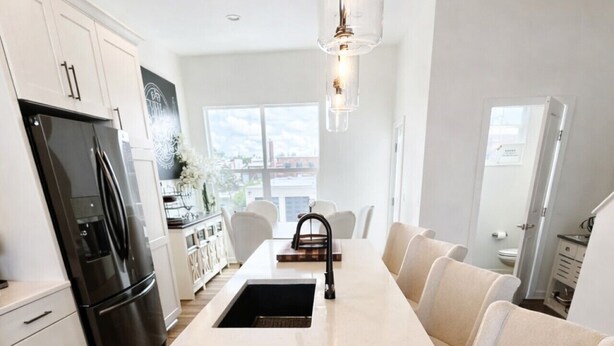 Une cuisine moderne dotée d’un îlot central, de meubles blancs, d’un réfrigérateur noir et d’un luminaire suspendu.