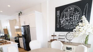 Une cuisine moderne avec des meubles blancs, un réfrigérateur noir et un coin repas comprenant une table ronde en bois et des chaises blanches.