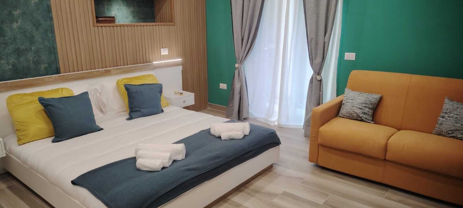 A bedroom with a bed, bedside table, nightstand, and a sofa.