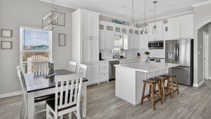 Une cuisine moderne avec des meubles blancs, un îlot central, des appareils électroménagers en acier inoxydable et un coin repas comprenant une table et des chaises.