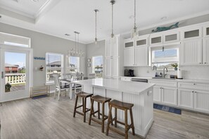 A spacious kitchen with white cabinetry, a large island with stools, pendant lighting, and a view through the windows.