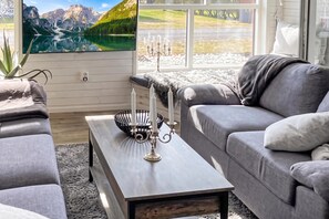 Una sala de estar moderna con un sofá gris, una mesa de centro de madera y un ventanal con vistas a la montaña.