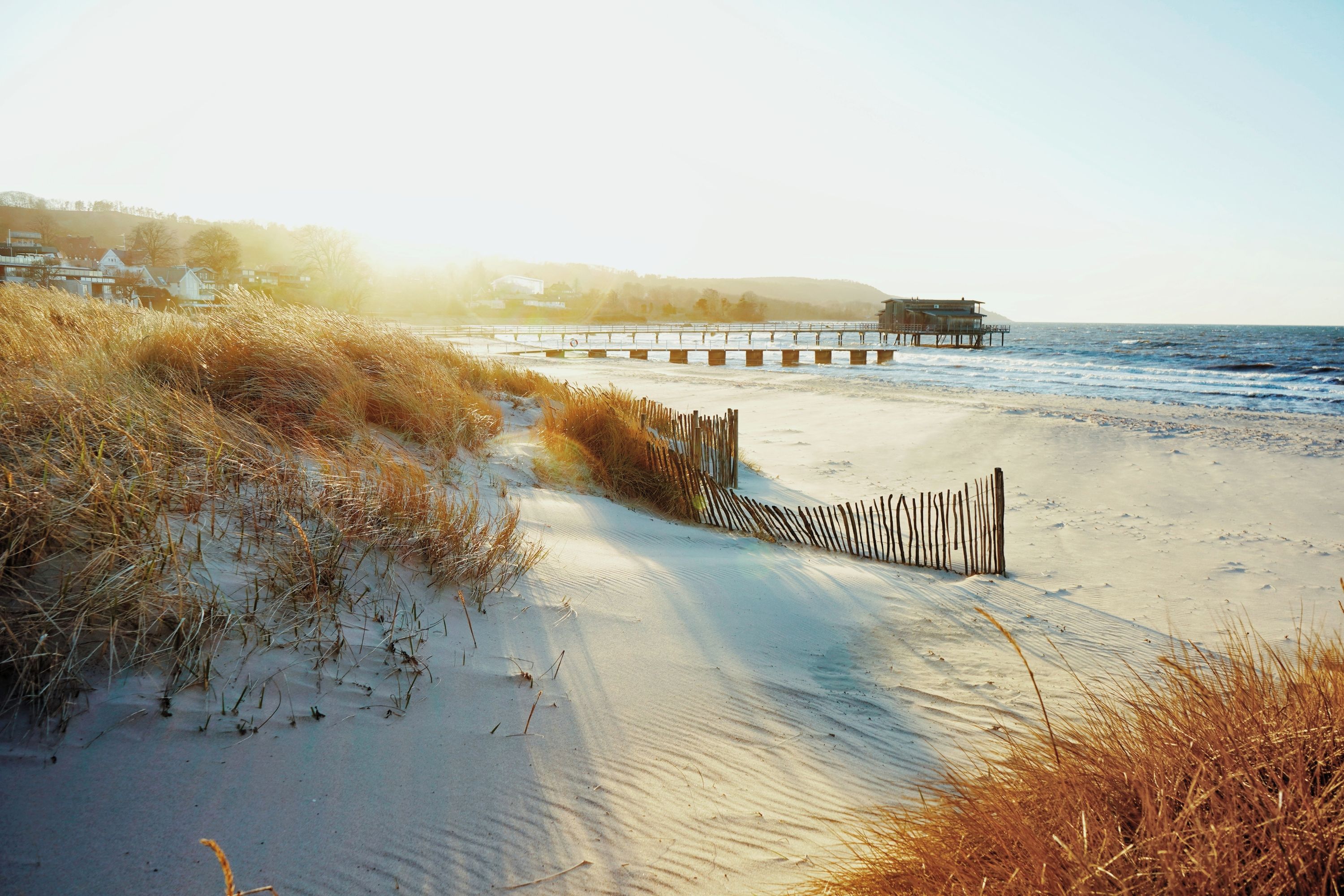 A sandy beach with a wooden fence and a pier extending into the water.