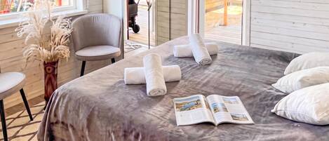 A bedroom with a bed, pillows, a chair, a table, and a window.