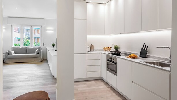 Una cocina moderna con armarios blancos, horno empotrado y pileta de acero inoxidable.