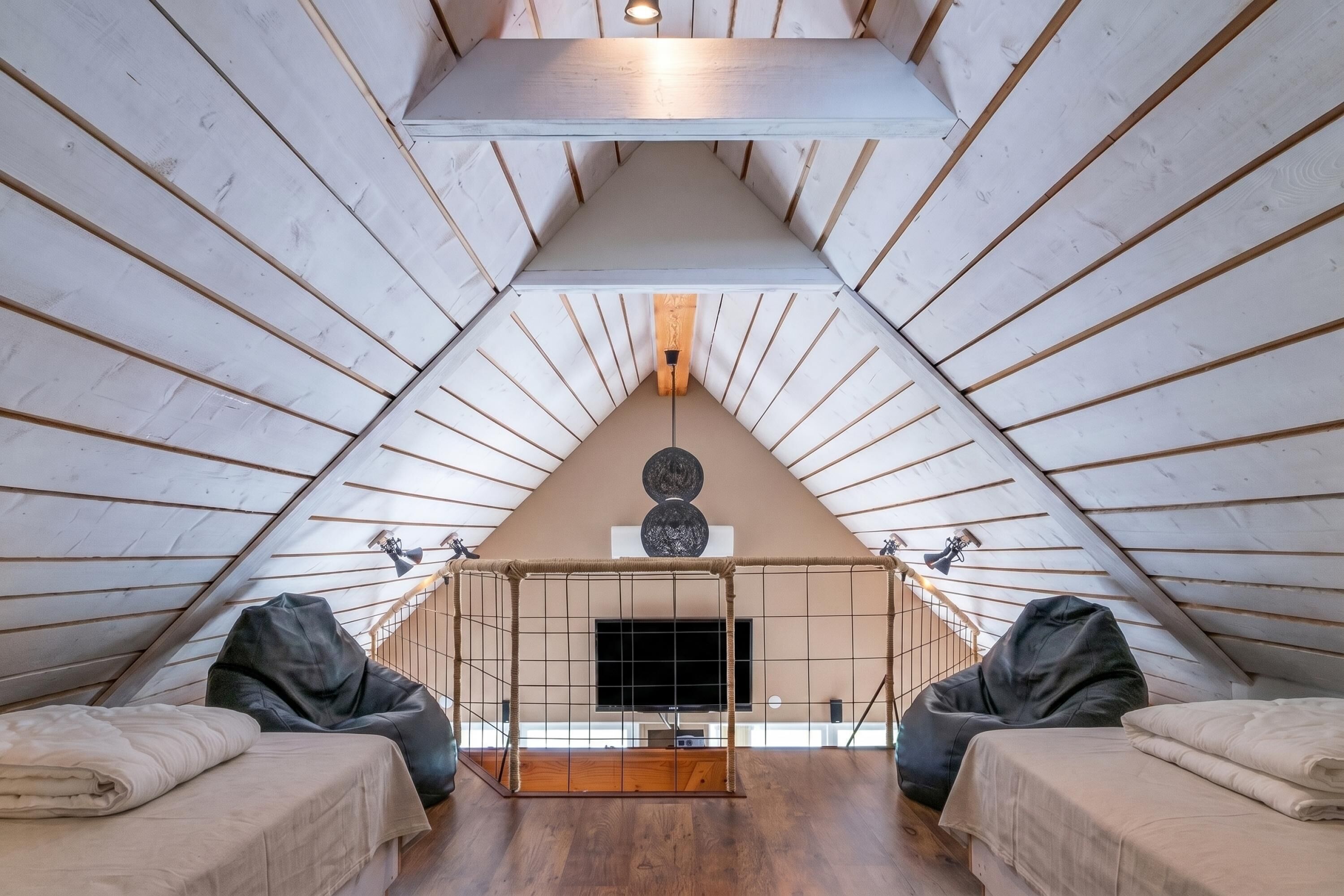 An attic bedroom with a sloped ceiling, a TV, two bean bags, and a fireplace.