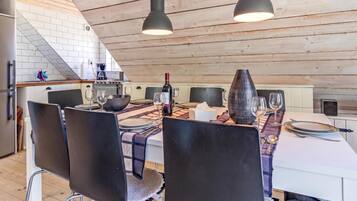 Un coin repas avec une table dressée pour quatre personnes, des chaises, une bouteille de vin et un vase.
