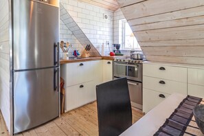 A compact kitchen with a stainless steel refrigerator, wooden cabinets, a black chair, and a dining table. - Aspö Island Hideaway Family Home 80, Drottningskär, Sweden (Drottningskär)