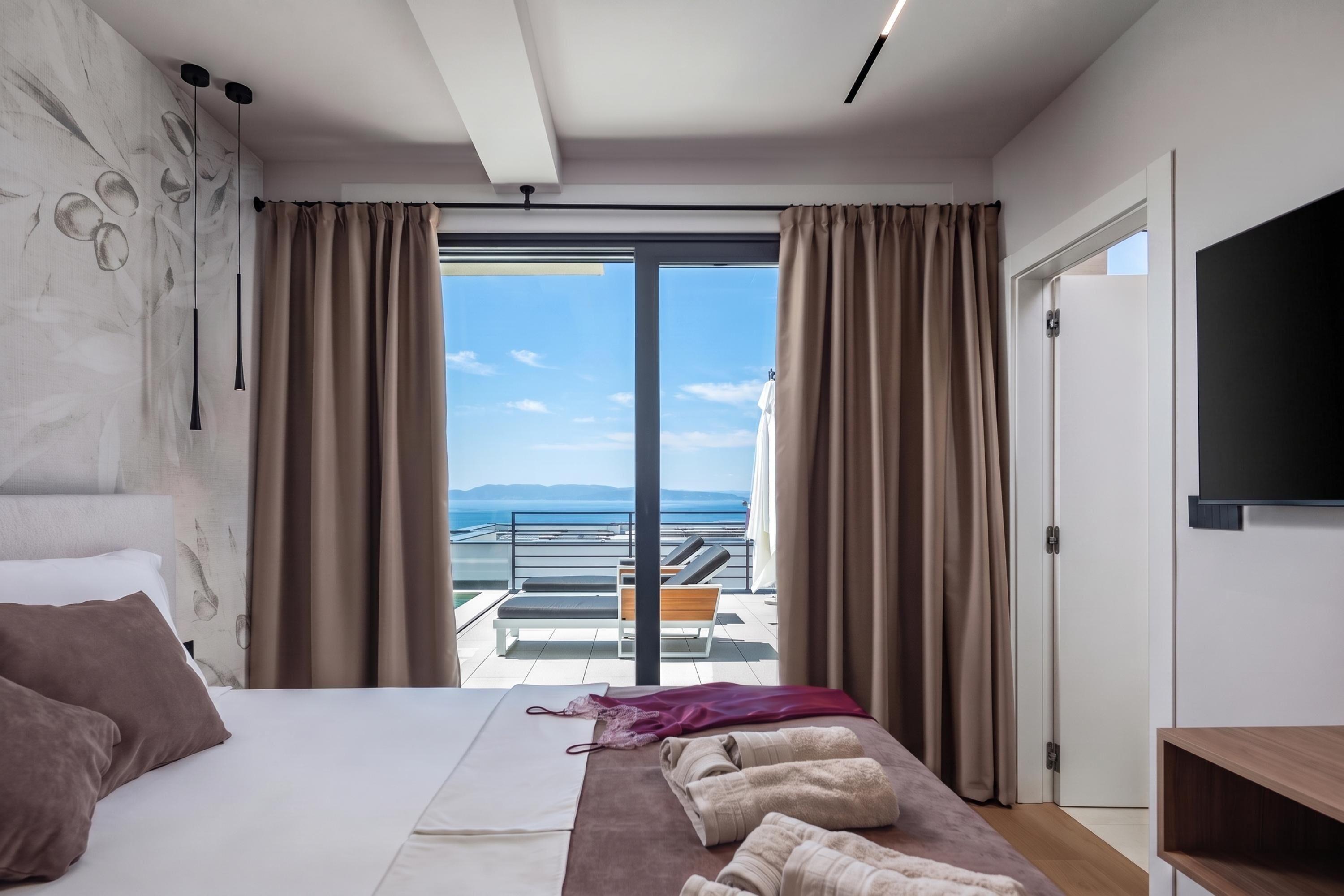 Une chambre d’hôtel avec un lit, une banquette avec des serviettes, une télévision et un balcon offrant une vue.