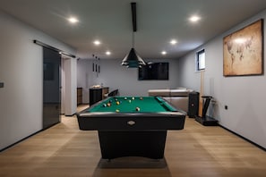 Ein Billardtisch in einem modernen Raum mit einer Couch, einem Fernseher und einer Weltkarte an der Wand.
