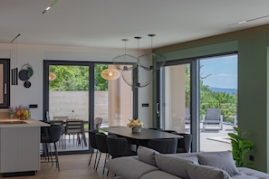 Ein modernes Interieur mit Essbereich, einer Couch und großen Fenstern.