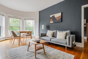 A modern living room with a grey sofa, a wooden coffee table, and a dining area with chairs and a table. - Blueground | Back Bay West, city view, nr Charles River (Boston)