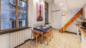A dining area with a table set for four, wooden chairs, a painting of a tower, a staircase, and a kitchen area. - Da Stefano Historical Center 5 min to Aquarium, Genova, Italy (Genova)