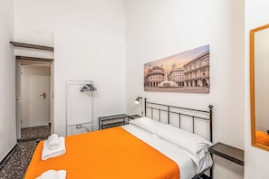 Ein Hotelzimmer mit Bett, Nachttisch, Lampe, einem Bild eines Gebäudes und einer Tür.