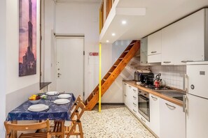 Eine kleine Küche mit weißen Schränken, einer Holztreppe und einem Essbereich mit Tisch für zwei Personen.