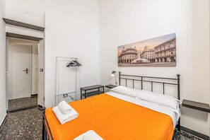 Ein Hotelzimmer mit Bett, Nachttisch, Lampe, Kleiderständer und einem Gemälde eines historischen Gebäudes.
