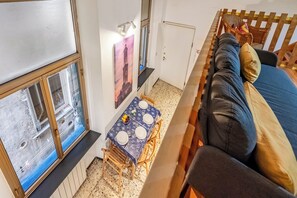 Ein Zimmer mit einem hölzernen Bett, einem Esstisch mit Stühlen, einem Fenster mit Jalousien und einem an der Wand hängenden Bild.