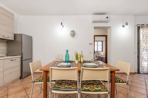 A modern kitchen with a dining area, featuring a stainless steel refrigerator, a wooden table set for four, and a clock on the wall. - Le Dimore Del Sole, Olbia, Italy (Olbia)