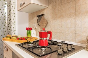 A kitchen with a gas stove, a red kettle, a tray with food items, and a wooden cutting board. - Le Dimore Del Sole, Olbia, Italy (Olbia)