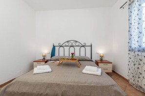 A neatly made bed with a tray of food, two bedside tables with lamps, and a window with a floral curtain. - Le Dimore Del Sole, Olbia, Italy (Olbia)
