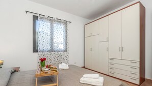 Een slaapkamer met een bed, een kledingkast, een raam met gordijnen, een nachtkastje met een dienblad en een schilderij op de vloer.