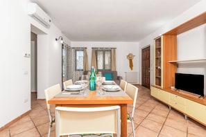 A dining area with a table set for four, a television on a wooden stand, and a wardrobe with a mirror. - Le Dimore Del Sole, Olbia, Italy (Olbia)