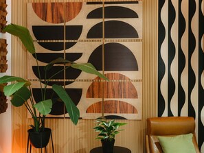 Una habitación con diseño geométrico en la pared, un sillón de cuero marrón y dos macetas con plantas.