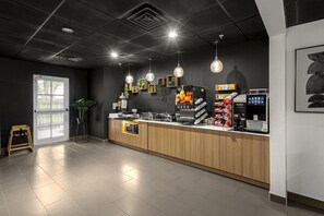 Una cafetería moderna con un mostrador de madera, máquinas de espresso e iluminación colgante.