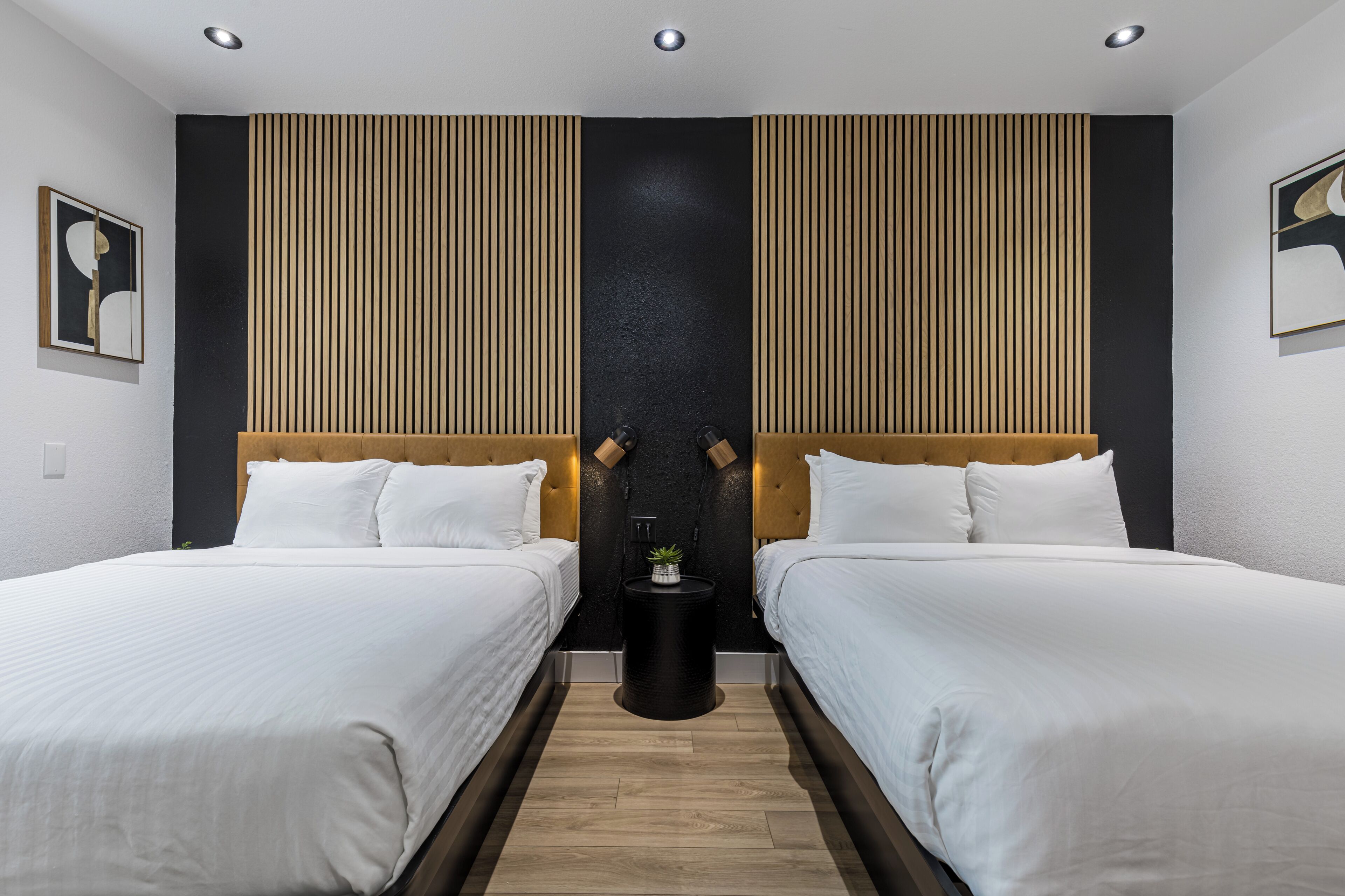 A modern hotel room with two beds, a black accent wall, and a small side table with a plant.