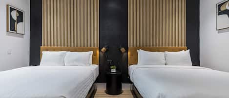 A modern hotel room with two beds, a black accent wall, and a small side table with a plant.