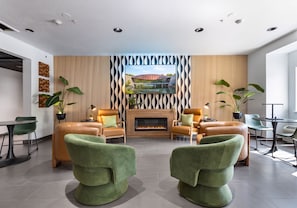 Una sala de estar moderna con chimenea, sofás de cuero verde y marrón, un televisor de pantalla plana y una pared con un diseño estampado.