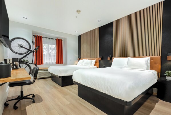 Ein modernes Hotelzimmer mit zwei Betten, einem Schreibtisch, einem Stuhl und einem Fahrrad.