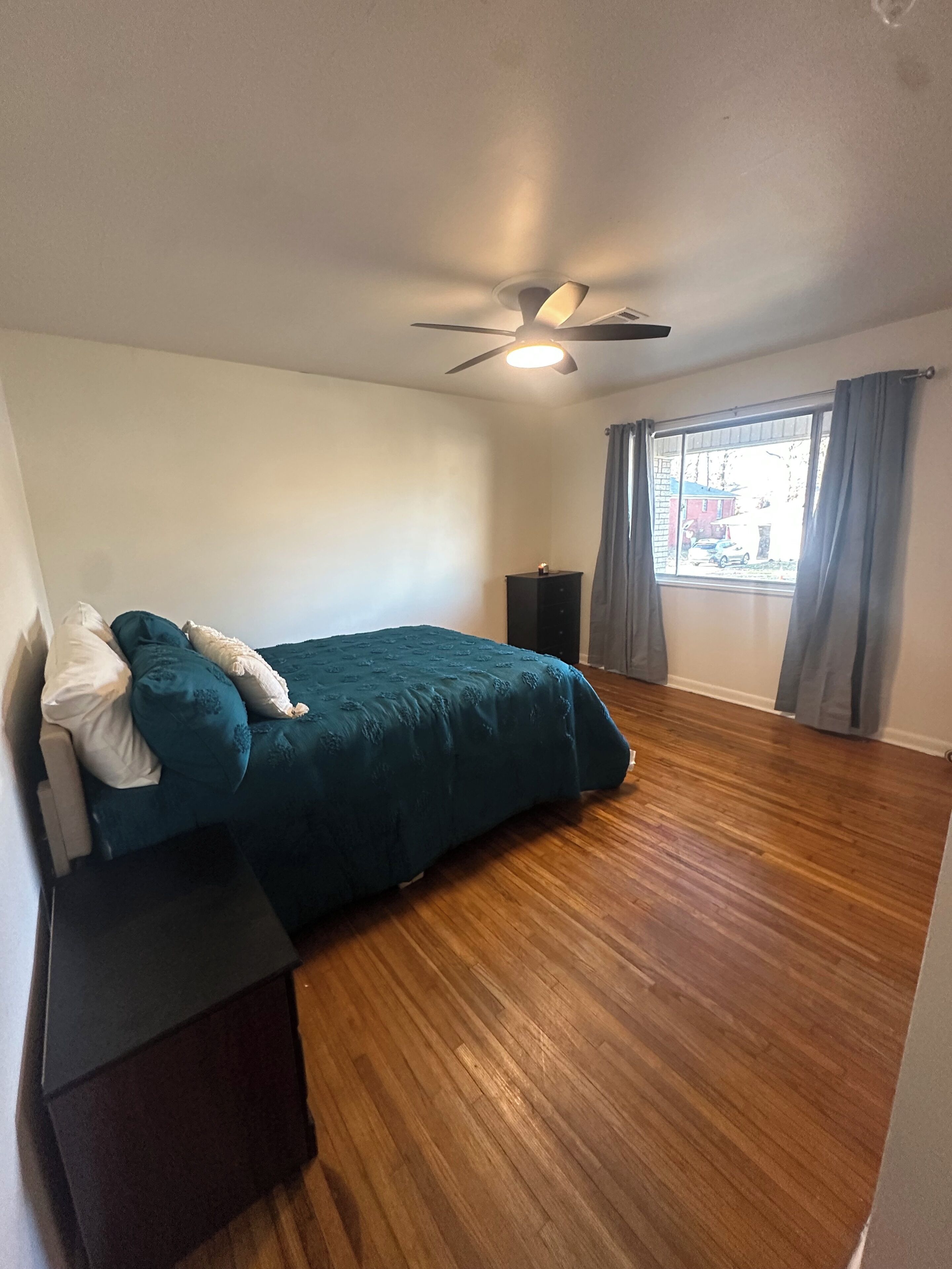 A bedroom with a bed, a ceiling fan, a window with curtains, and a speaker.