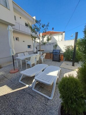 Eine Terrasse mit zwei Liegestühlen, einem Tisch und einem Grill.