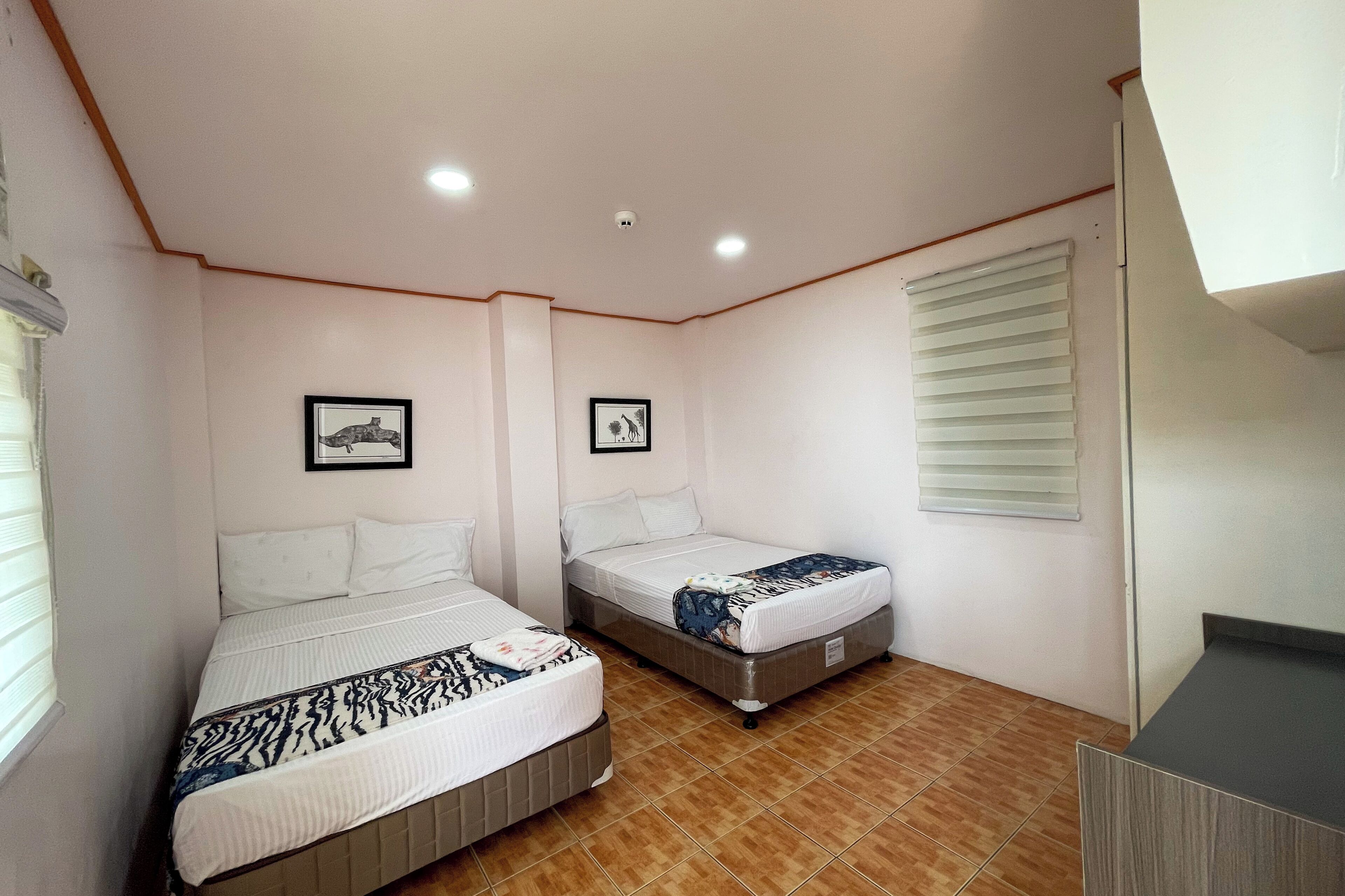 Un dormitorio con dos camas, una ventana con persianas e iluminación empotrada en el techo.