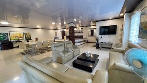 A spacious living area with a sofa, armchairs, a coffee table, a TV, and artwork on the walls.