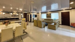 A modern living room with a dining area, a sofa set, and a kitchen in the background.