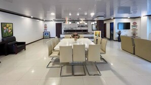 A modern dining area with a large rectangular table, multiple chairs, and a kitchen in the background.