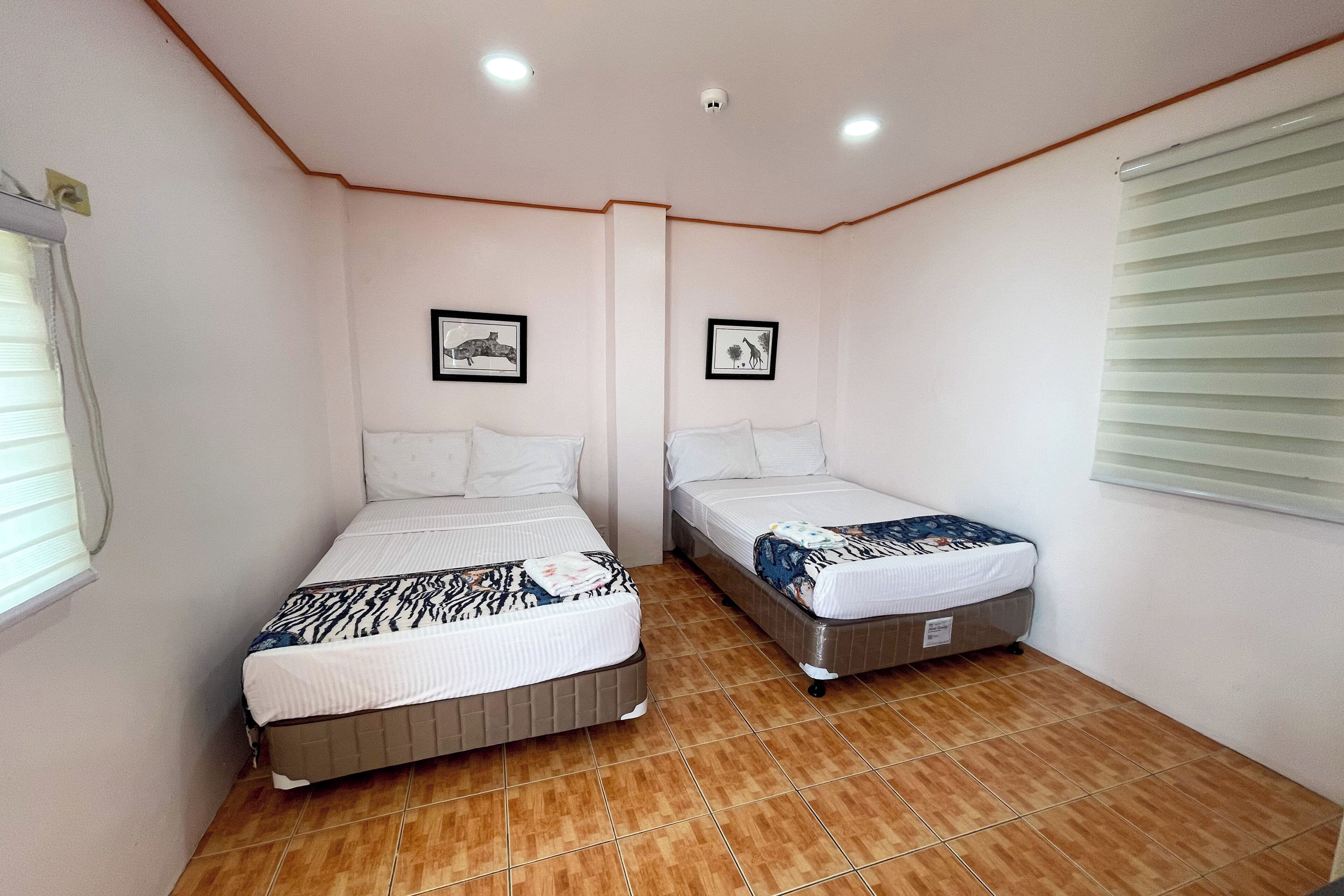 A room with two beds, a ceiling fan, and a window with blinds.